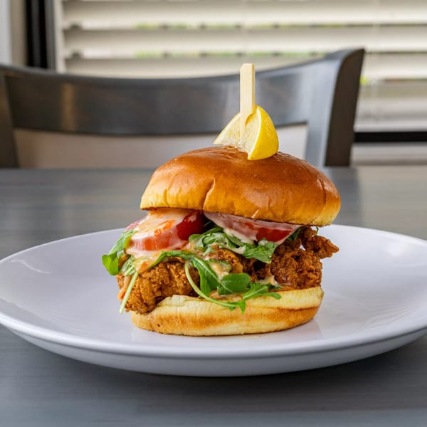 Hutchinson Island Bar and Grille's fried chicken sandwich with arugula, tomatoes, and sauce on a brioche bun.