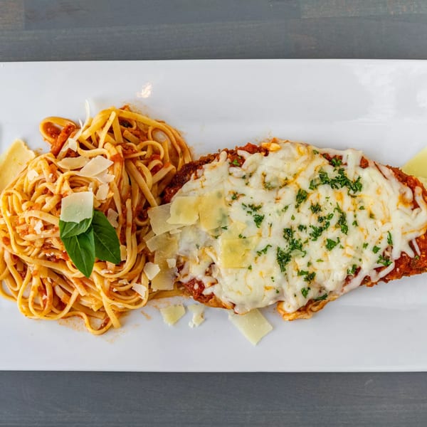 Chicken parmesan with melted cheese and parsley, alongside linguine pasta with red sauce and basil.