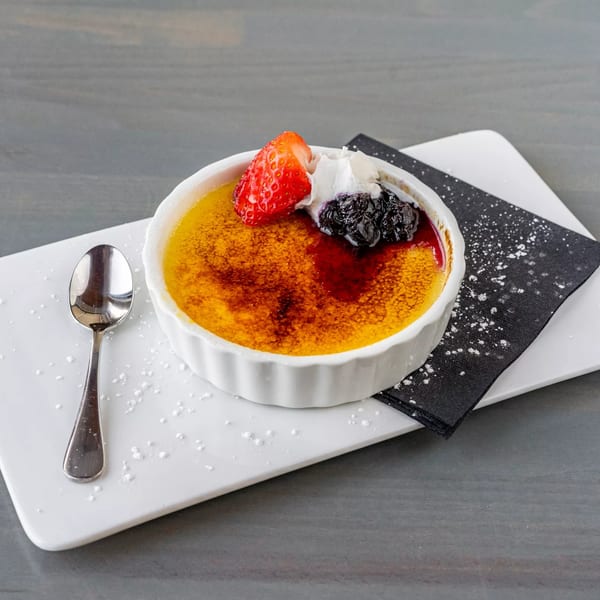 Hutchinson Island Bar and Grille's creme brulee with berries, whipped cream, and a spoon on a white plate.