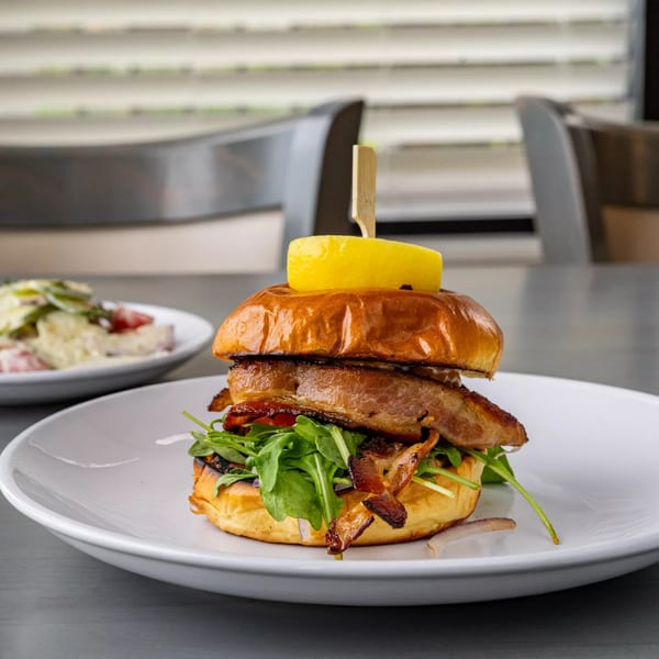 A gourmet burger with thick bacon, arugula, and a lemon slice on a brioche bun.