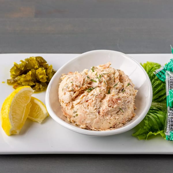 Salmon dip with dill, lemon wedges, chopped jalapeños, and lettuce on a white platter.