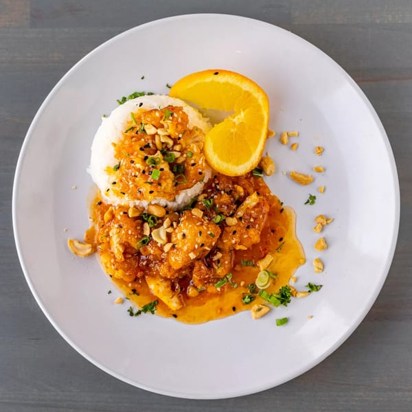 Orange chicken with white rice, garnished with sesame seeds, cashews, and green onions.