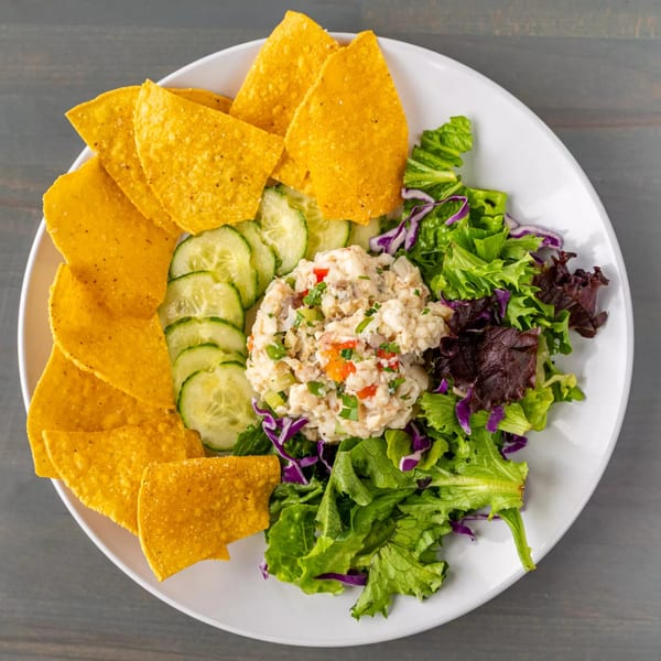 A white plate with ceviche, tortilla chips, sliced cucumbers, and mixed greens.